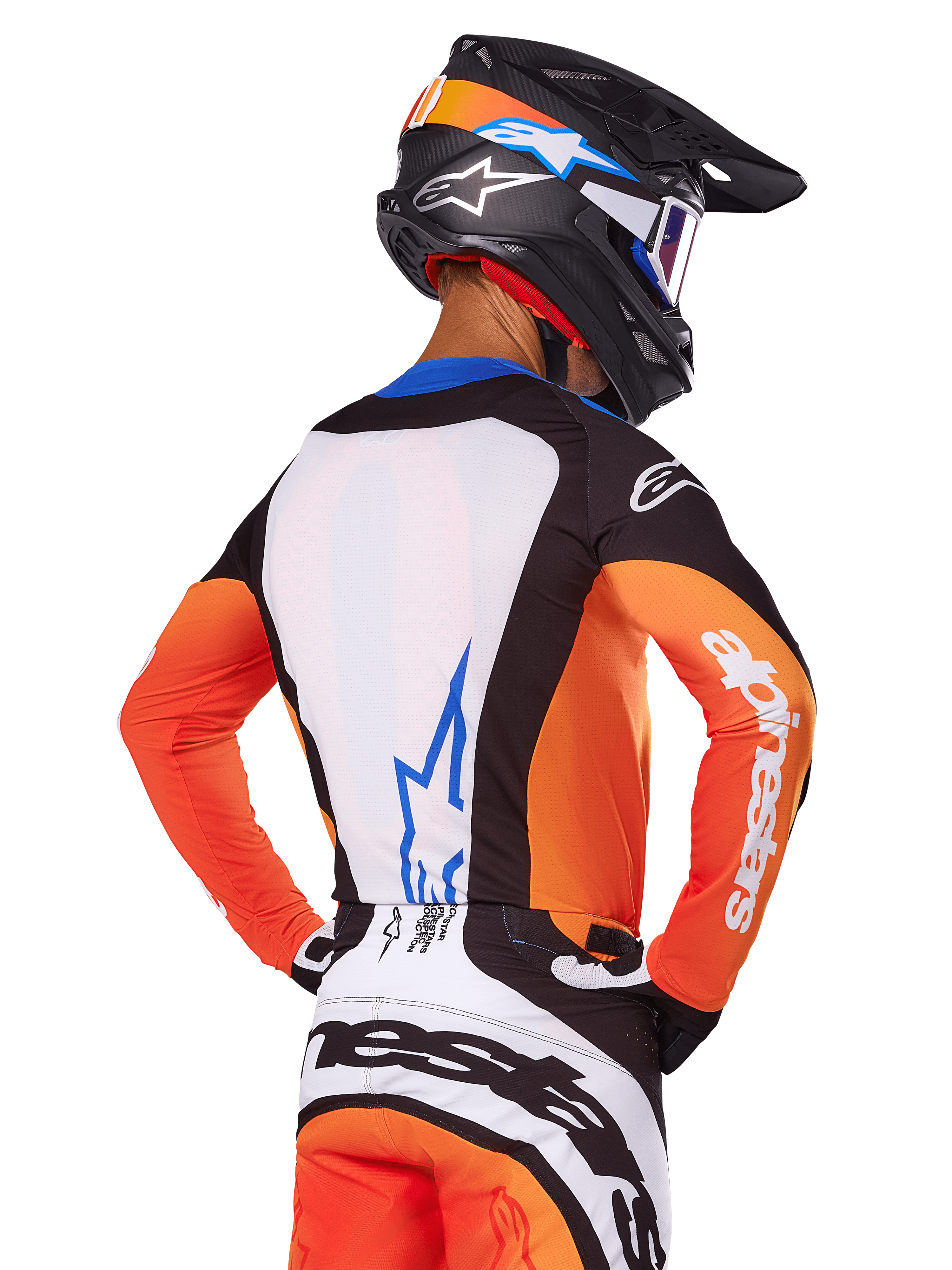 Pilote de motocross portant le maillot Alpinestars Techstar Melt 2025, orange et bleu, vue de dos montrant un panneau dorsal blanc avec logo bleu, manches oranges avec marquage blanc, casque et pantalon de motocross assortis, équipement de course professionnel