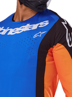Alpinestars Techstar Melt Jersey 2025, maillot de motocross, bleu et orange avec empiècements noirs, logo Alpinestars blanc et perforations découpées au laser visibles sur la poitrine, porté par un pilote avec un casque noir