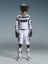 Maillot Alpinestars Racer Riway 2026, maillot de motocross, blanc et noir, porté comme une tenue de course complète avec pantalon assorti, casque noir avec lunettes rouges, gants noirs et bottes blanches, arborant le marquage 'astars' noir et des logos d'étoiles.