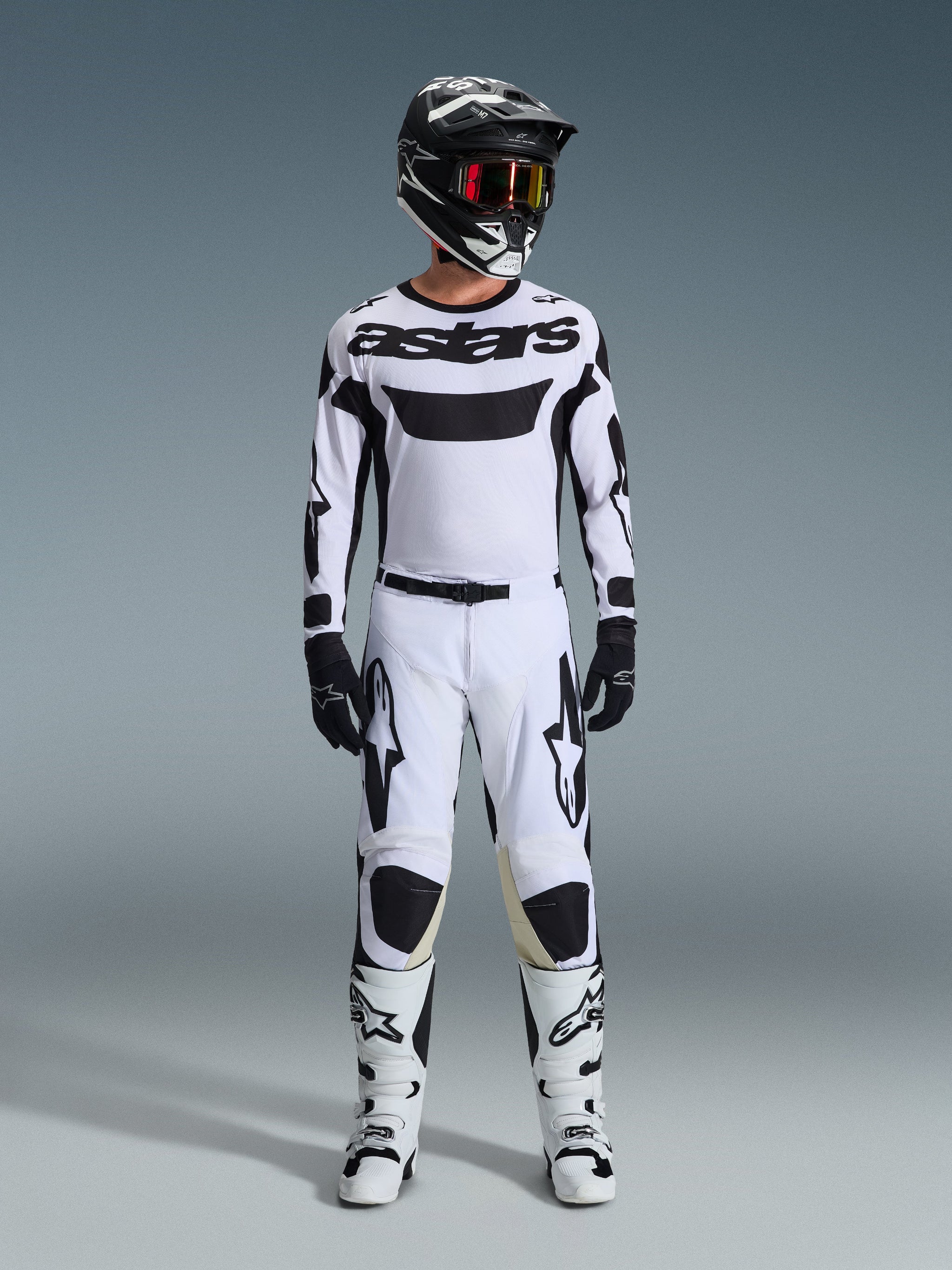 Maillot Alpinestars Racer Riway 2026, maillot de motocross, blanc et noir, porté comme une tenue de course complète avec pantalon assorti, casque noir avec lunettes rouges, gants noirs et bottes blanches, arborant le marquage 'astars' noir et des logos d'étoiles.