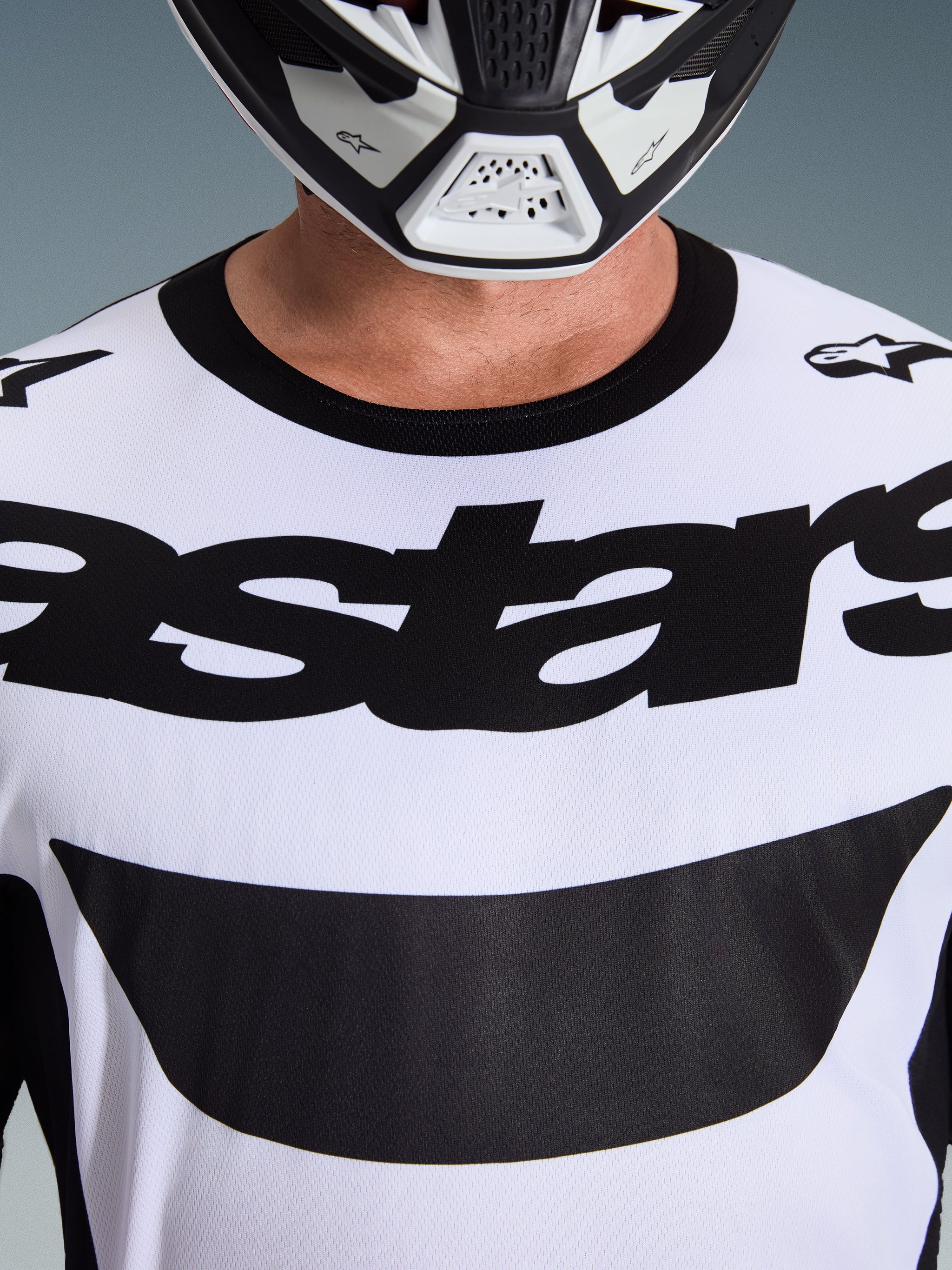 Maillot Alpinestars Racer Riway 2026, maillot de motocross, blanc et noir, gros plan sur le torse présentant un logo Astars noir imposant et un col noir, porté avec un casque blanc et noir, équipement de pilotage tout-terrain haute performance