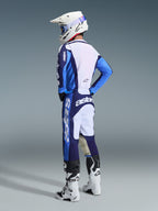 Pilote de motocross vu de trois-quarts arrière portant l'ensemble Alpinestars Racer Riway 2026 en bleu UCLA et blanc, composé d'un maillot bleu et blanc avec marquage « astars », d'un pantalon assorti, d'un casque de motocross blanc avec lunettes bleues et de bottes de la série Tech blanches et noires.