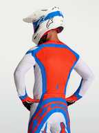 Alpinestars Maillot Supertech Vesta, maillot de motocross pour homme, rouge, bleu et blanc, avec perforations laser respirantes, vue de dos sur un mannequin avec casque, équipement de performance tout-terrain