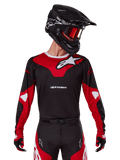 Alpinestars 2025 Racer Veil Jersey, maillot de motocross, noir et rouge vif, porté avec un pantalon assorti, un casque noir et des lunettes rouges, arborant des logos blancs audacieux et un design de course épuré, équipement de performance pour le motocross tout-terrain