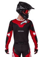 Alpinestars 2025 Racer Veil Jersey, maillot de motocross, noir et rouge vif, porté avec un pantalon assorti, un casque noir et des lunettes rouges, arborant des logos blancs audacieux et un design de course épuré, équipement de performance pour le motocross tout-terrain