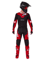 Pilote de motocross portant la tenue Alpinestars 2025 Racer Veil, maillot noir et rouge vif avec logo Alpinestars blanc, pantalon de motocross assorti, casque noir avec lunettes rouges et bottes rouges, équipement de performance complet pour la conduite tout-terrain