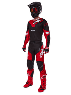 Pilote de motocross portant une tenue de course complète comprenant le maillot Alpinestars 2025 Racer Veil noir et rouge vif, un pantalon assorti, des bottes rouges, un casque noir avec des lunettes rouges et des gants rouges et noirs, look de performance coordonné pour la course tout-terrain