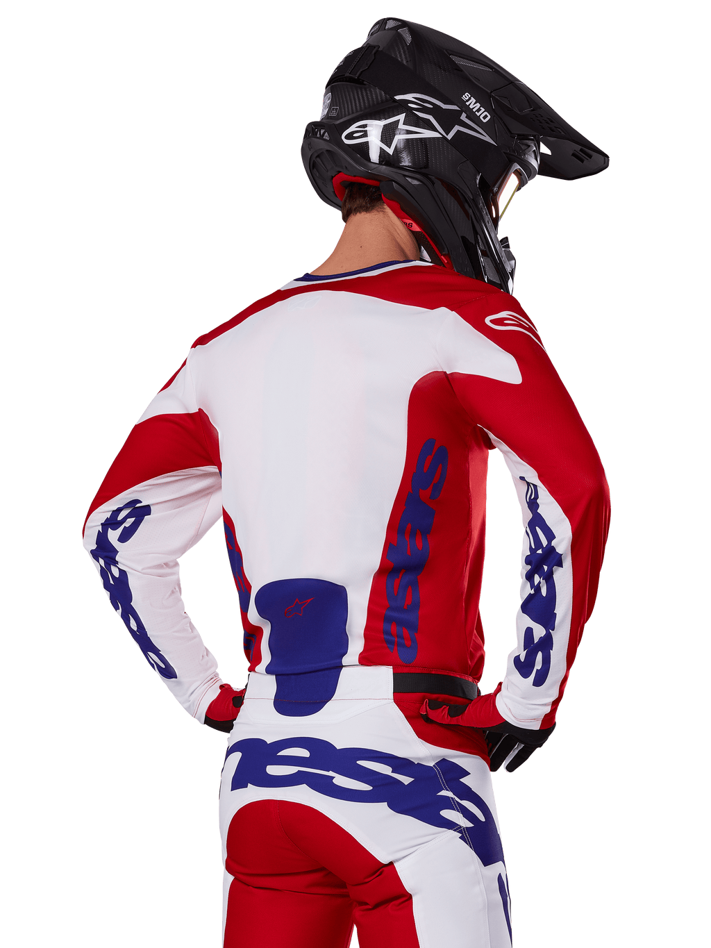 Ensemble maillot et pantalon Alpinestars Racer Veil 2025, tenue de motocross, rouge vif, blanc et bleu, vue arrière d'un pilote portant l'équipement coordonné et un casque de motocross noir, arborant le logo Alpinestars bleu, vêtement technique de course tout-terrain
