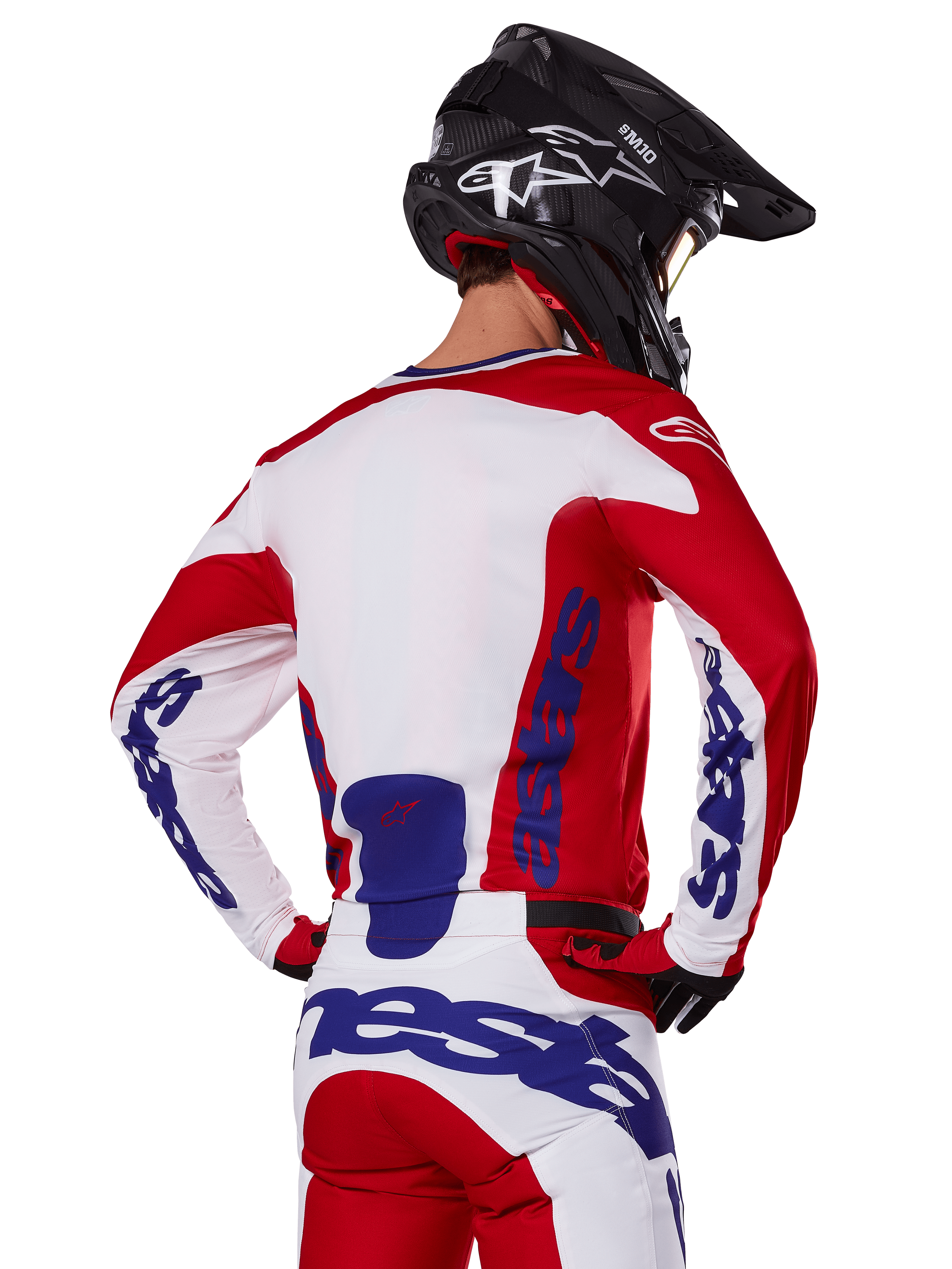 Ensemble maillot et pantalon Alpinestars Racer Veil 2025, tenue de motocross, rouge vif, blanc et bleu, vue arrière d'un pilote portant l'équipement coordonné et un casque de motocross noir, arborant le logo Alpinestars bleu, vêtement technique de course tout-terrain