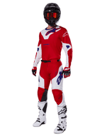 Ensemble d'équipement Alpinestars Racer Veil 2025, tenue de motocross rouge vif et blanc avec accents de logo bleus, porté avec un casque noir, des gants rouges et des bottes blanches, ensemble de protection complet pour performance tout-terrain