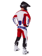 Pilote de motocross vu de dos portant le maillot et le pantalon Alpinestars Racer Veil 2025 en rouge et blanc, avec logos bleus, casque noir et bottes blanches, tenue complète pour la course tout-terrain