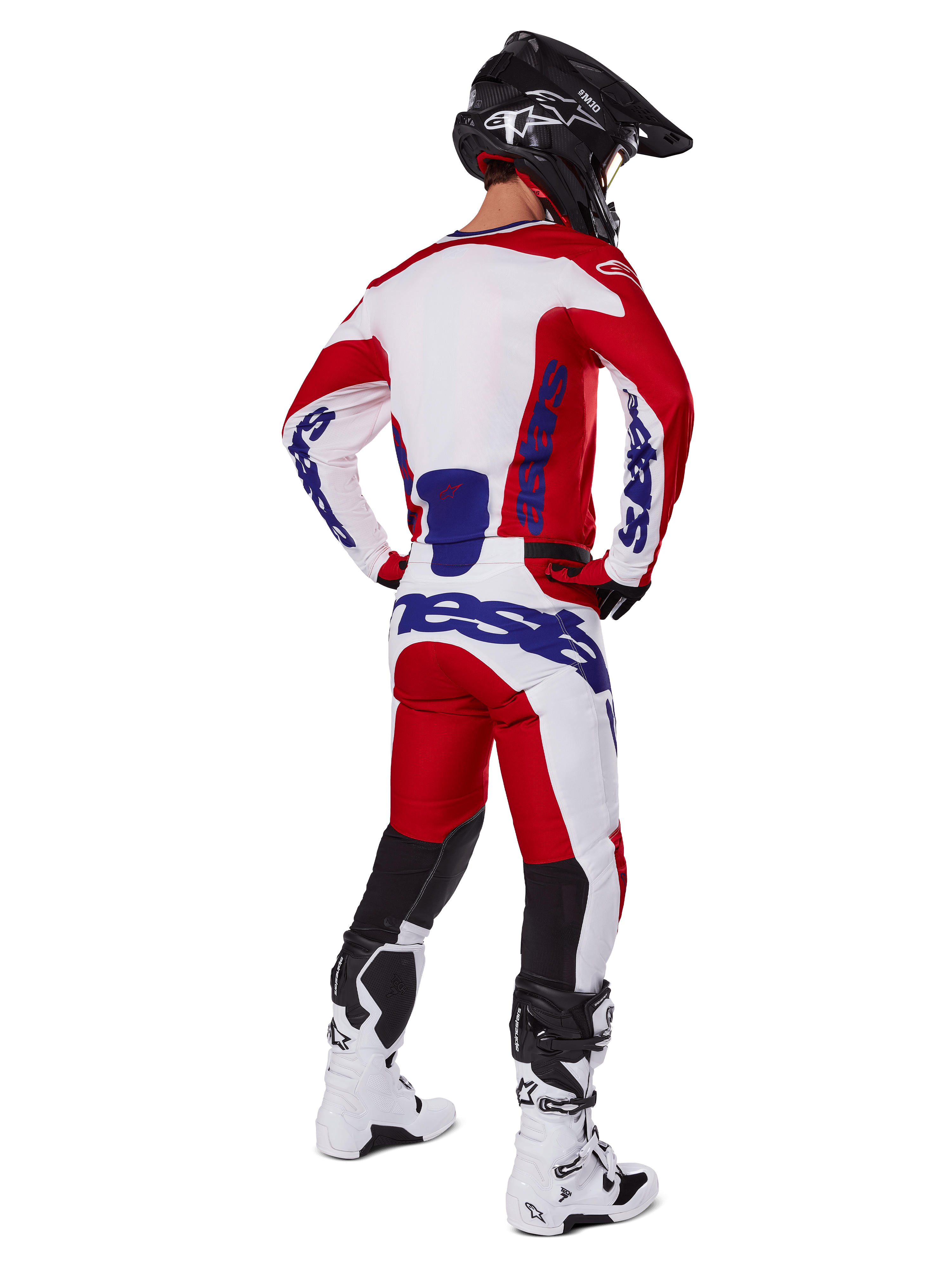 Pilote de motocross vu de dos portant le maillot et le pantalon Alpinestars Racer Veil 2025 en rouge et blanc, avec logos bleus, casque noir et bottes blanches, tenue complète pour la course tout-terrain