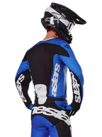 Set d'équipement Alpinestars Racer Veil 2025, équipement de motocross, bleu, noir et blanc, vue arrière d'un pilote portant un maillot et un pantalon avec un branding audacieux, casque noir et blanc, tenue coordonnée pour la course tout-terrain