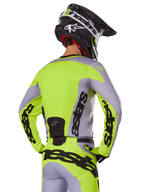 Motocross rider from behind wearing the Alpinestars 2025 Racer Veil Jersey in Gray and Yellow Fluo, featuring prominent 'astars' branding on the back and sleeves, paired with matching pants and a black helmet for a complete racing look.