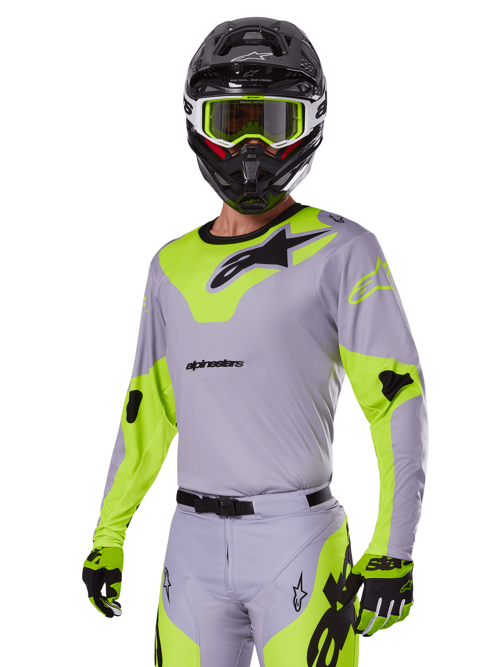 Pilote de motocross portant l'ensemble d'équipement Alpinestars Racer Veil 2025 en gris et vert fluo, maillot et pantalon gris clair avec des empiècements jaune-vert fluo vifs et des logos Alpinestars noirs, coordonné avec des gants assortis et un casque noir avec des lunettes vert fluo, tenue de course tout-terrain professionnelle.