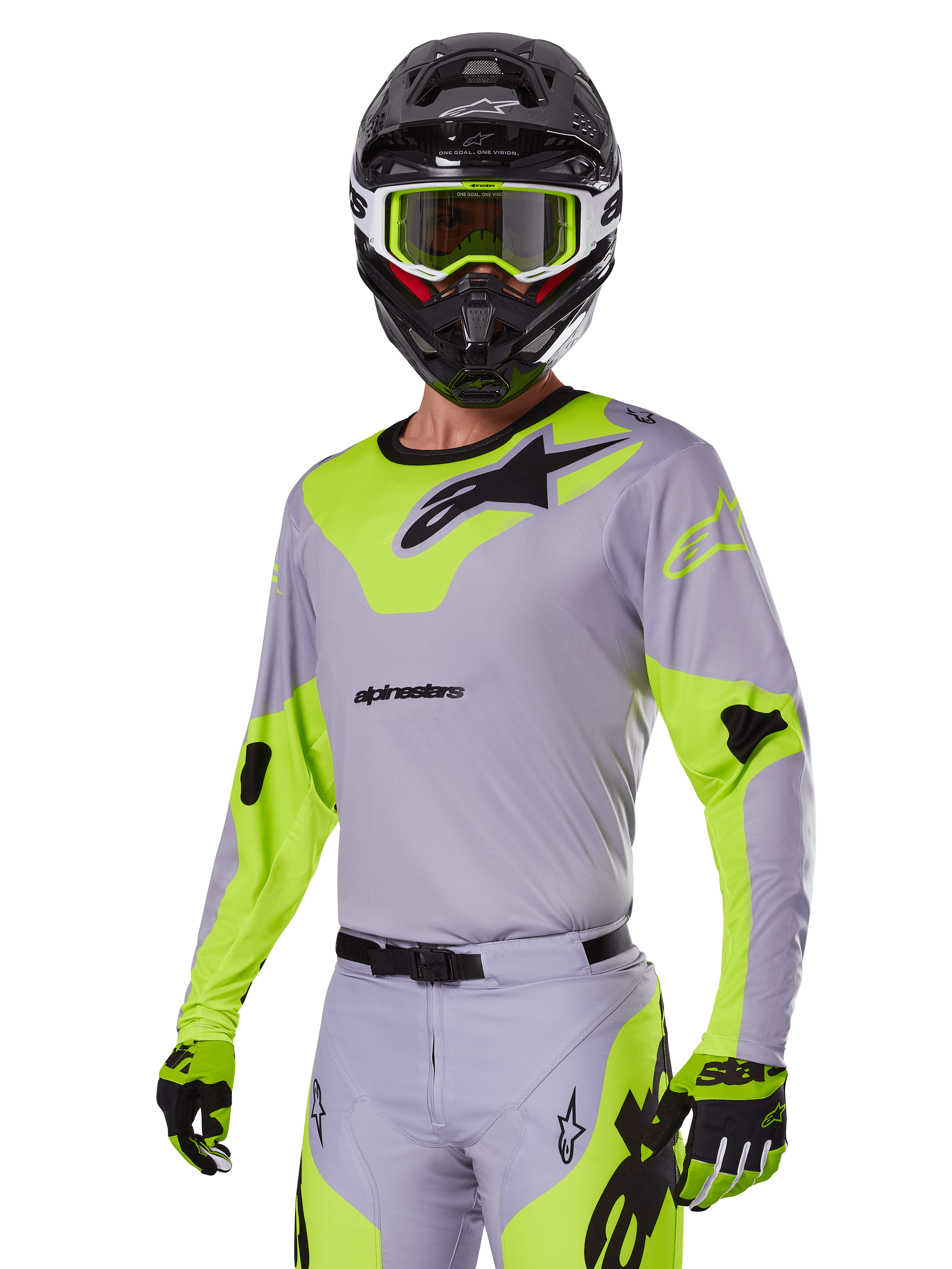 Pilote de motocross portant l'ensemble d'équipement Alpinestars Racer Veil 2025 en gris et vert fluo, maillot et pantalon gris clair avec des empiècements jaune-vert fluo vifs et des logos Alpinestars noirs, coordonné avec des gants assortis et un casque noir avec des lunettes vert fluo, tenue de course tout-terrain professionnelle.
