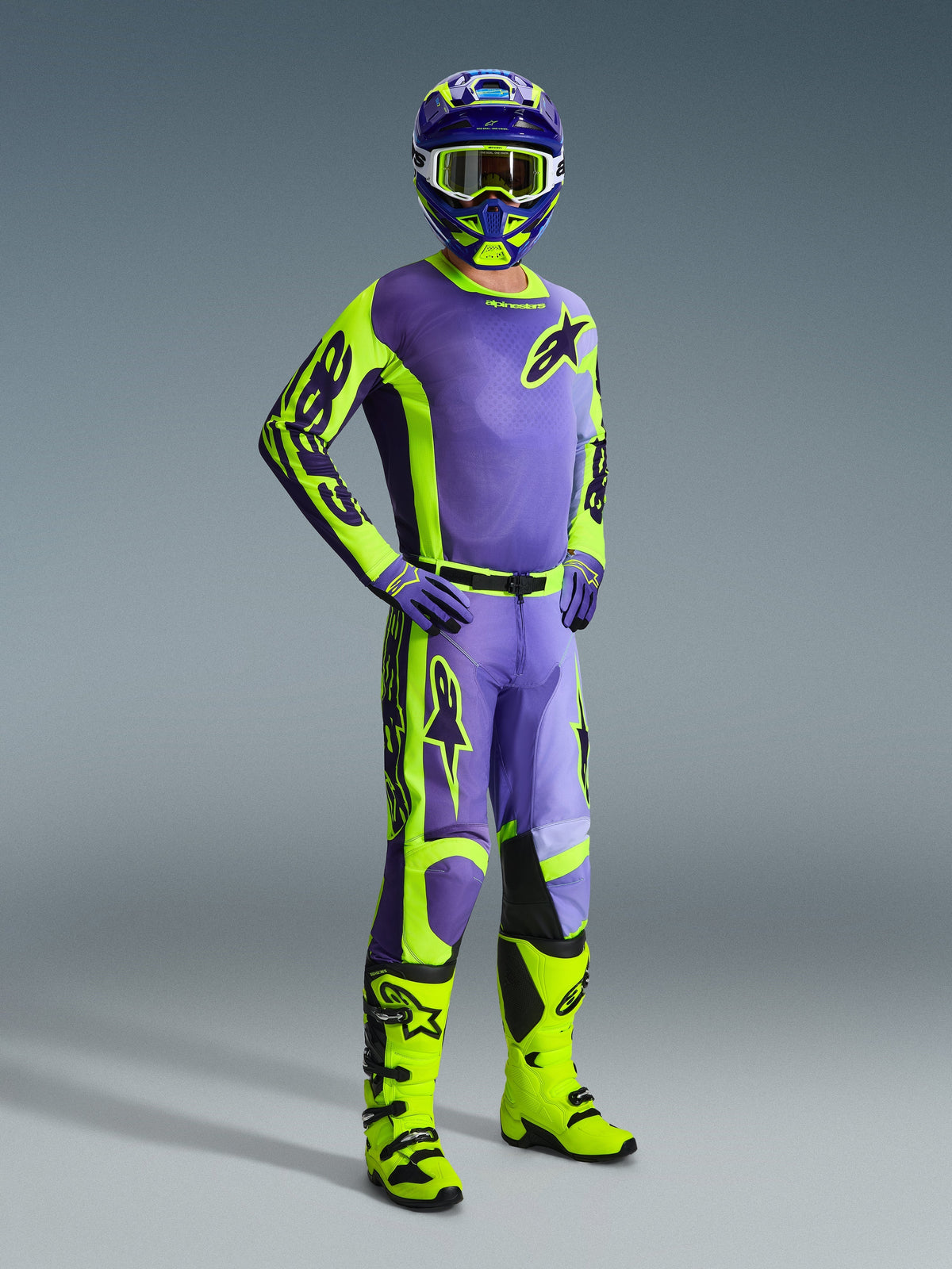 Pilote de motocross portant une tenue complète Alpinestars, comprenant le maillot Racer Portl 2026 et le pantalon assorti en violet et jaune fluo, avec casque, lunettes et gants violets coordonnés, complété par des bottes tout-terrain jaune fluo vif, tenue de course professionnelle pour la performance en motocross
