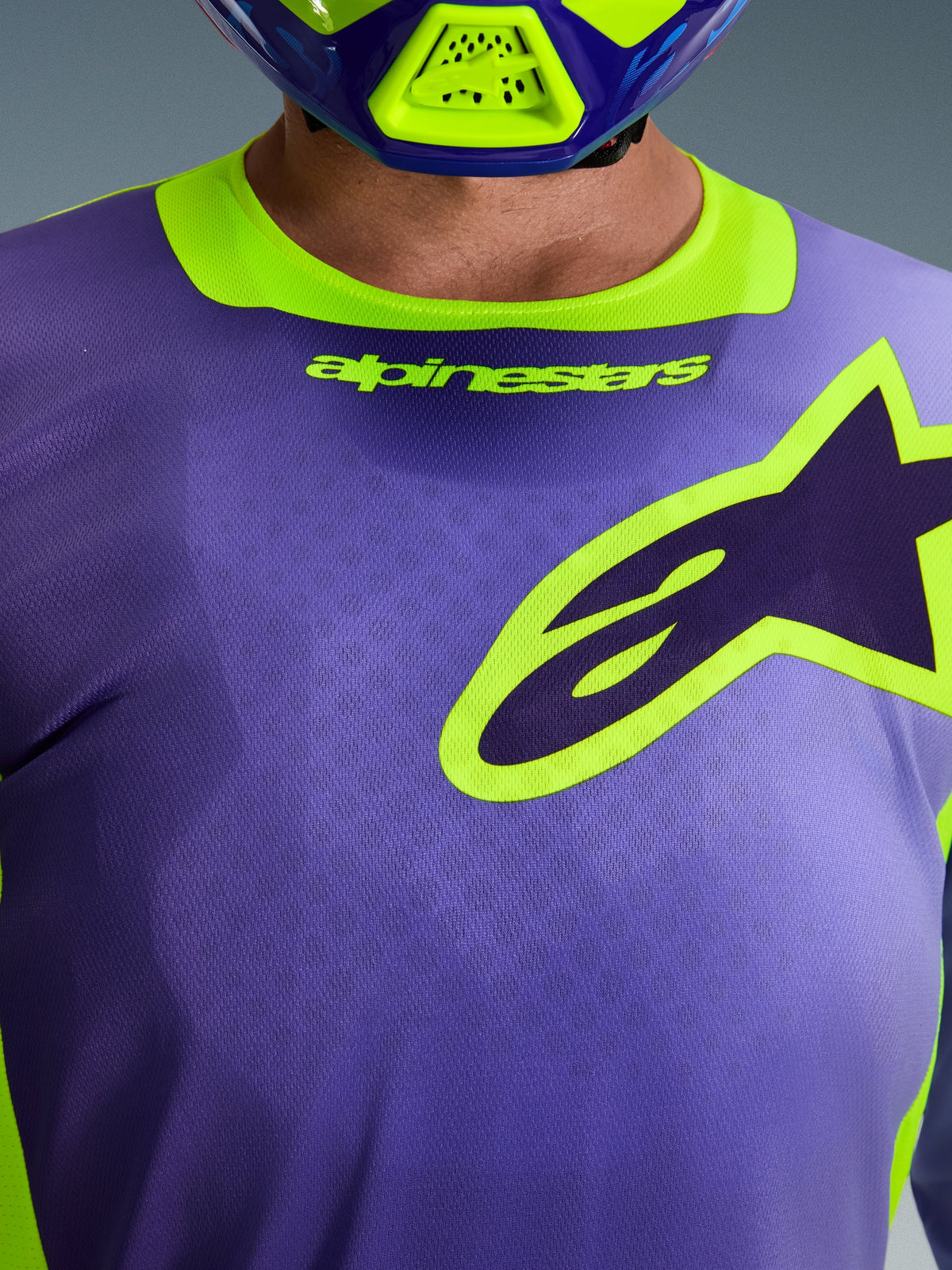 Maillot Alpinestars Racer Portl 2026, maillot de motocross, violet et jaune fluo, gros plan sur la poitrine avec un grand logo Alpinestars aux contours jaunes, col extensible avec marquage, tissu technique en poly-tissu évacuant l'humidité