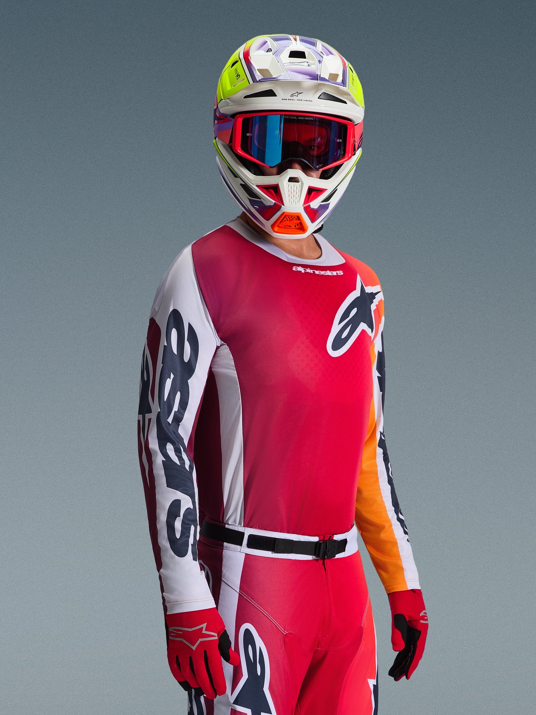 Pilote de motocross portant le maillot Racer Portl 2026, rouge avec des manches blanches et gris foncé, associé à un pantalon de motocross assorti, un casque multicolore avec des lunettes bleues et des gants rouges, photo en studio