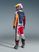 Pilote de motocross portant une tenue de course complète vue de dos, maillot Alpinestars 2026 Racer Portl en rouge, gris clair et vert foncé avec empiècements orange et bordeaux, pantalon assorti blanc et rouge, bottes grises et noires avec détails roses, casque multicolore, tenue de course tout-terrain coordonnée.