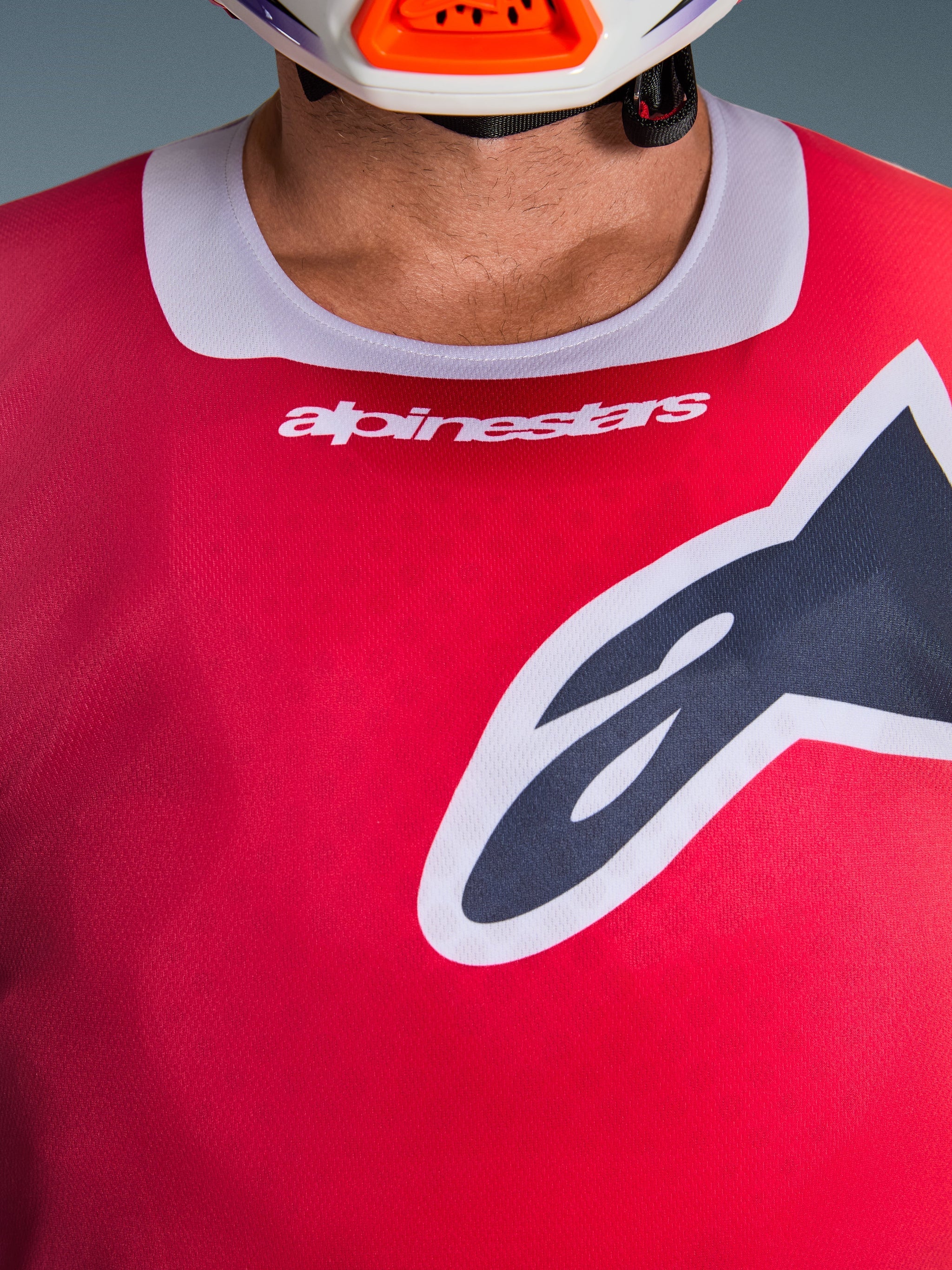 Gros plan sur le maillot Alpinestars Racer Portl 2026 en rouge, doté d'un col extensible gris clair avec marquage blanc et d'un grand logo Astars noir sur la poitrine, équipement de motocross haute performance