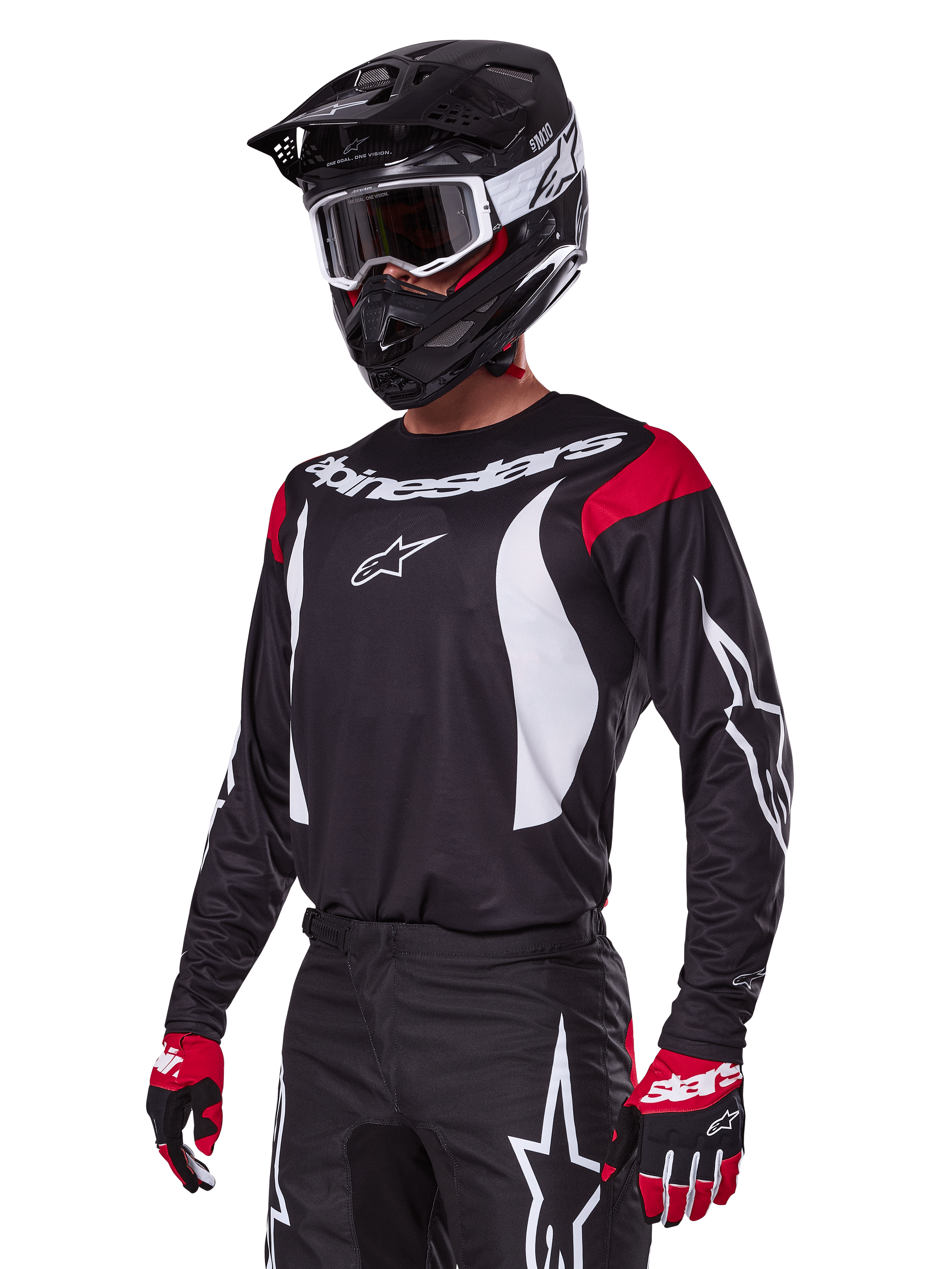 Pilote de motocross portant l'ensemble d'équipement Alpinestars Fluid Haul 2025, maillot noir avec empiècements rouges aux épaules et graphismes blancs, pantalon noir assorti avec logos étoiles blancs, gants rouges et noirs, casque noir avec détails blancs et lunettes, tenue de motocross coordonnée.
