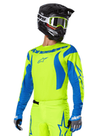Ensemble d'équipement Alpinestars Fluid Haul 2025, maillot et pantalon de motocross, jaune vif et bleu, porté avec un casque noir et des lunettes à monture jaune, présente des motifs bleus ondulés sur les manches et des logos d'étoiles bleues sur le pantalon, tenue de course tout-terrain coordonnée
