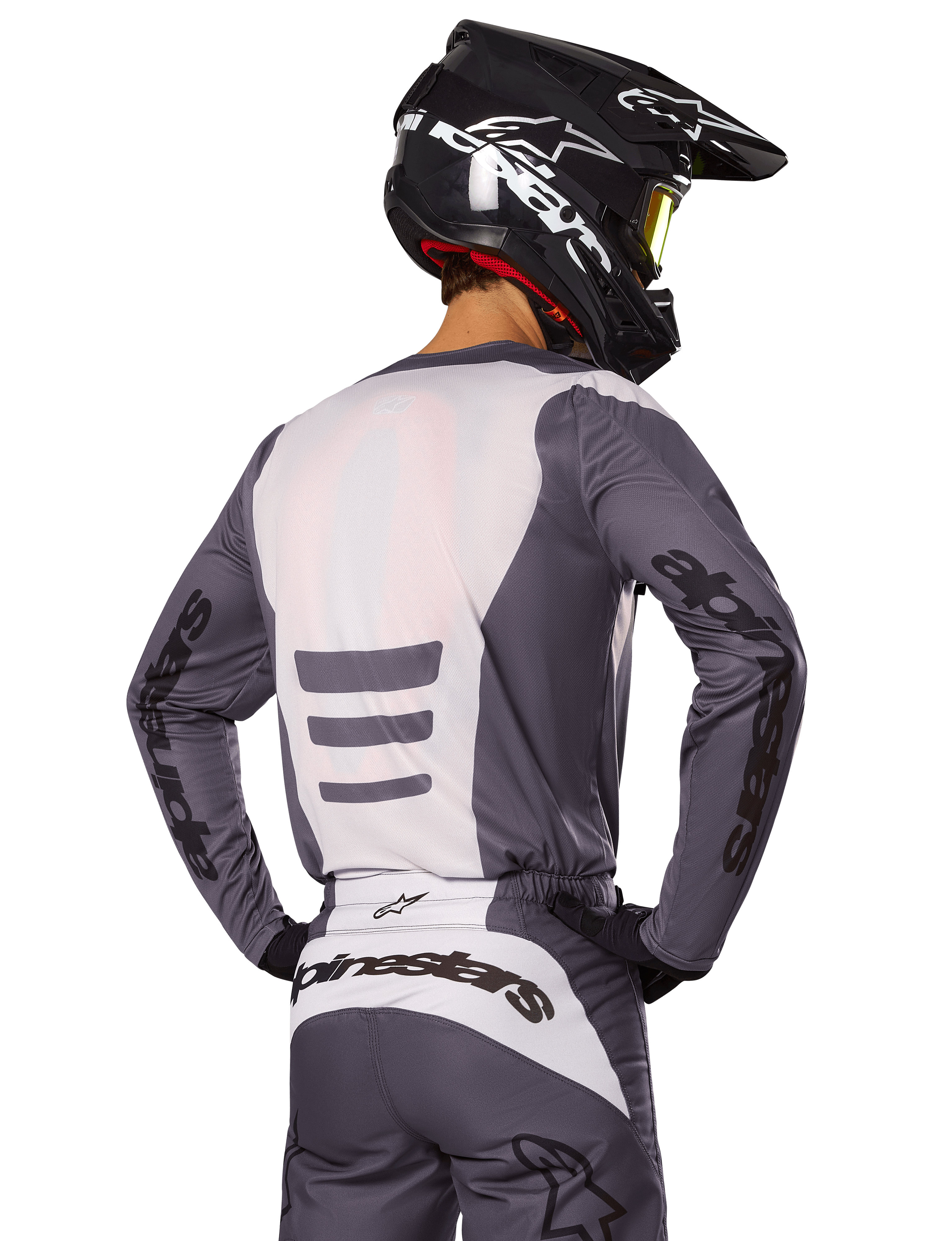 Motocross rider from behind wearing Alpinestars 2025 Fluid Haul Gear Set, Gray and White jersey and pants, black helmet with white graphics, yellow goggles, coordinated motocross racing outfit