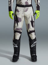 Alpinestars 2026 Racer Lahnd Pants, Motocross Pants, Sand Camo pattern with gray and purple abstract graphics, worn with neon yellow gloves and black boots, featuring black star logos on the thighs and a black waist belt, durable off-road racing gear