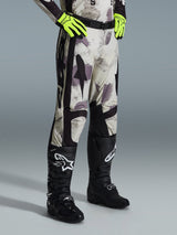 Alpinestars 2026 Racer Lahnd Pants, Motocross Pants, Sand Camo, worn with neon yellow gloves and black motocross boots, featuring an abstract camouflage pattern with black side panels, ergonomic off-road design