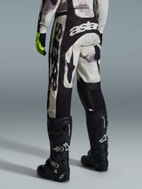 Alpinestars 2026 Racer Lahnd Pants, Motocross Pants, Sand Camo and Gray, rear view featuring bold white branding on the seat and legs, paired with black motocross boots and yellow gloves, professional off-road racing gear