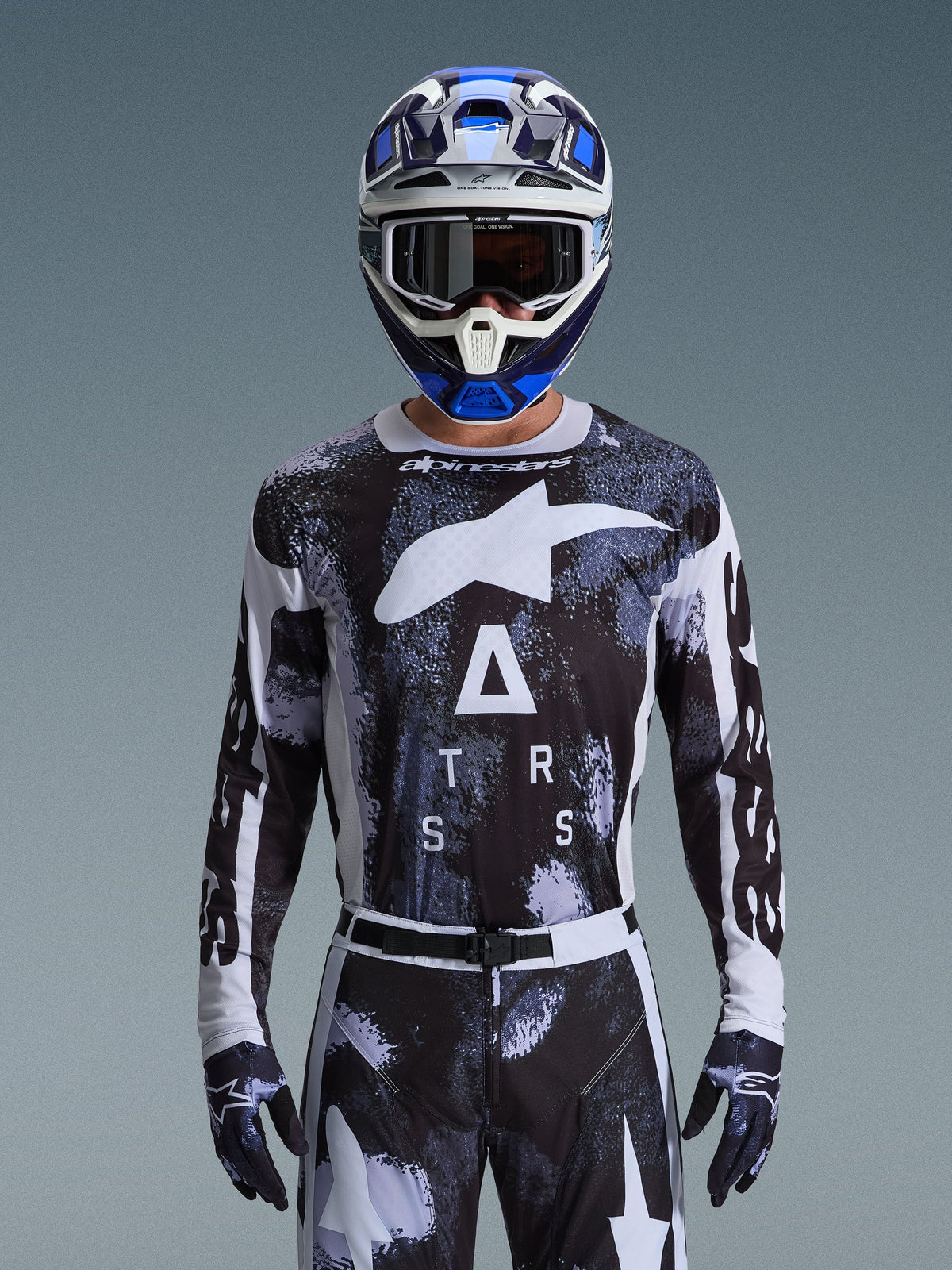Maillot Alpinestars Racer Lahnd 2026, équipement de motocross, motif Iron Camo noir et blanc, avec logo étoile et lettrage ASTARS, porté avec pantalon assorti et casque de motocross bleu