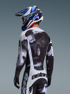 Ensemble d'équipement Alpinestars Racer Lahnd 2026, pilote de motocross vu de dos portant un maillot et un pantalon avec graphisme moucheté noir et blanc, associé à un casque bleu et blanc et des gants noirs, équipement de course tout-terrain haute performance
