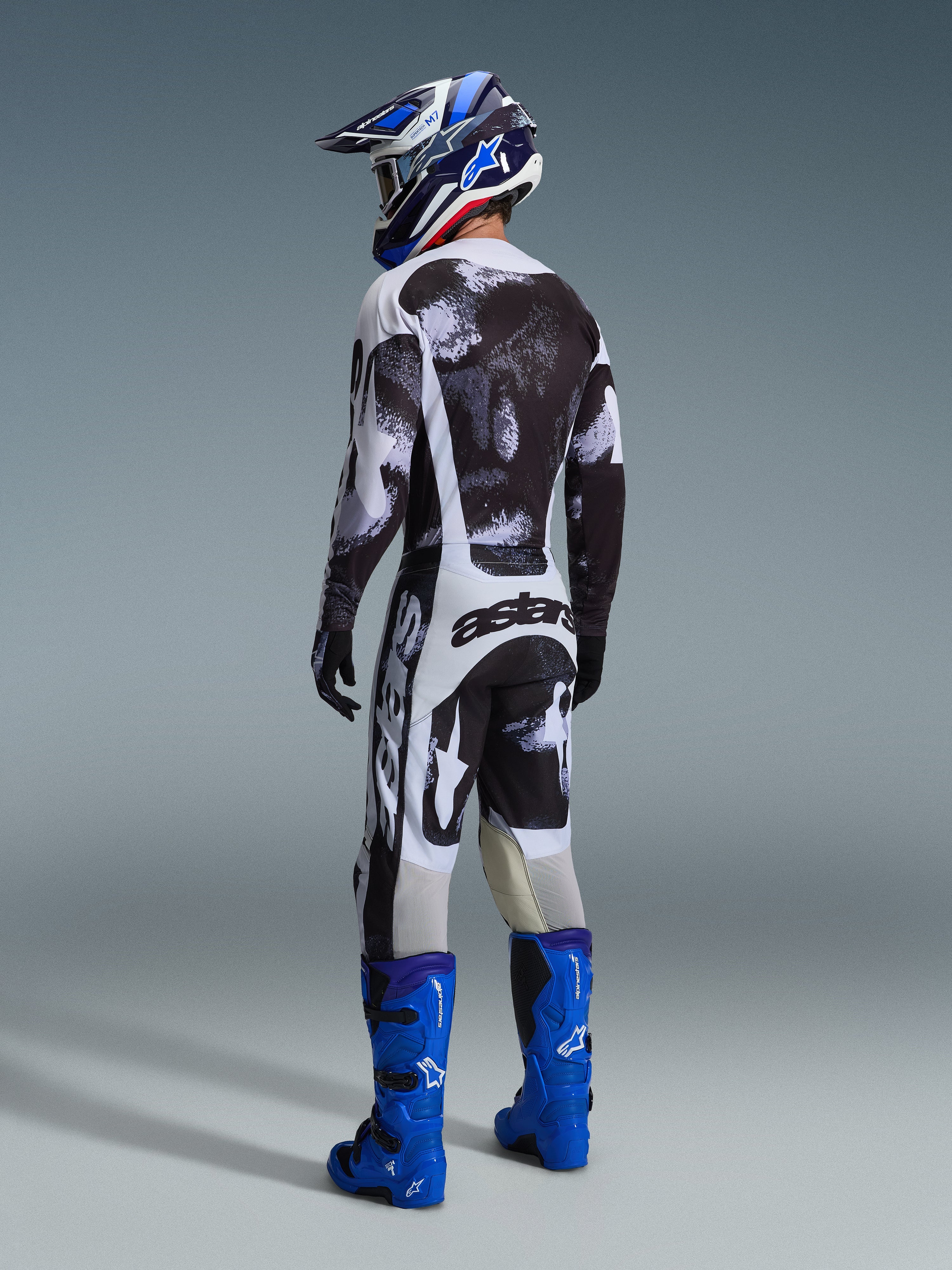 Ensemble d'équipement Alpinestars Racer Lahnd 2026, vue arrière d'un pilote de motocross, maillot et pantalon aux motifs abstraits noir et blanc, bottes et casque bleus, kit de course professionnel pour performance tout-terrain