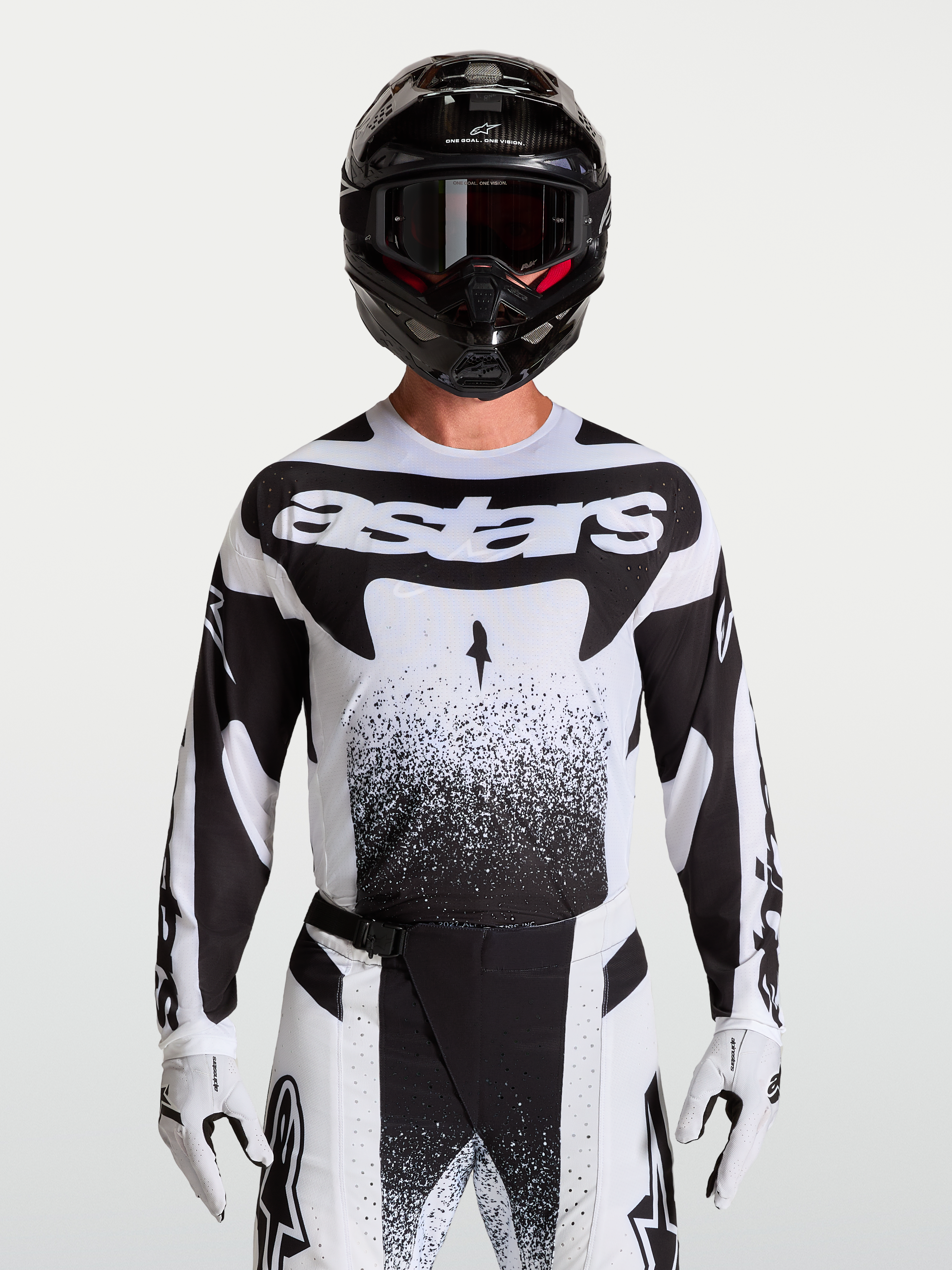 Maillot Alpinestars Techstar Swan, maillot de motocross pour homme, blanc et noir, coupe athlétique en tissu extensible léger avec perforations laser, porté par un mannequin avec casque et gants