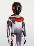 Maillot Alpinestars Techstar Swan, maillot de motocross pour homme, gris et rouge fluo, coupe athlétique extensible avec perforations laser pour la ventilation, porté par un pilote