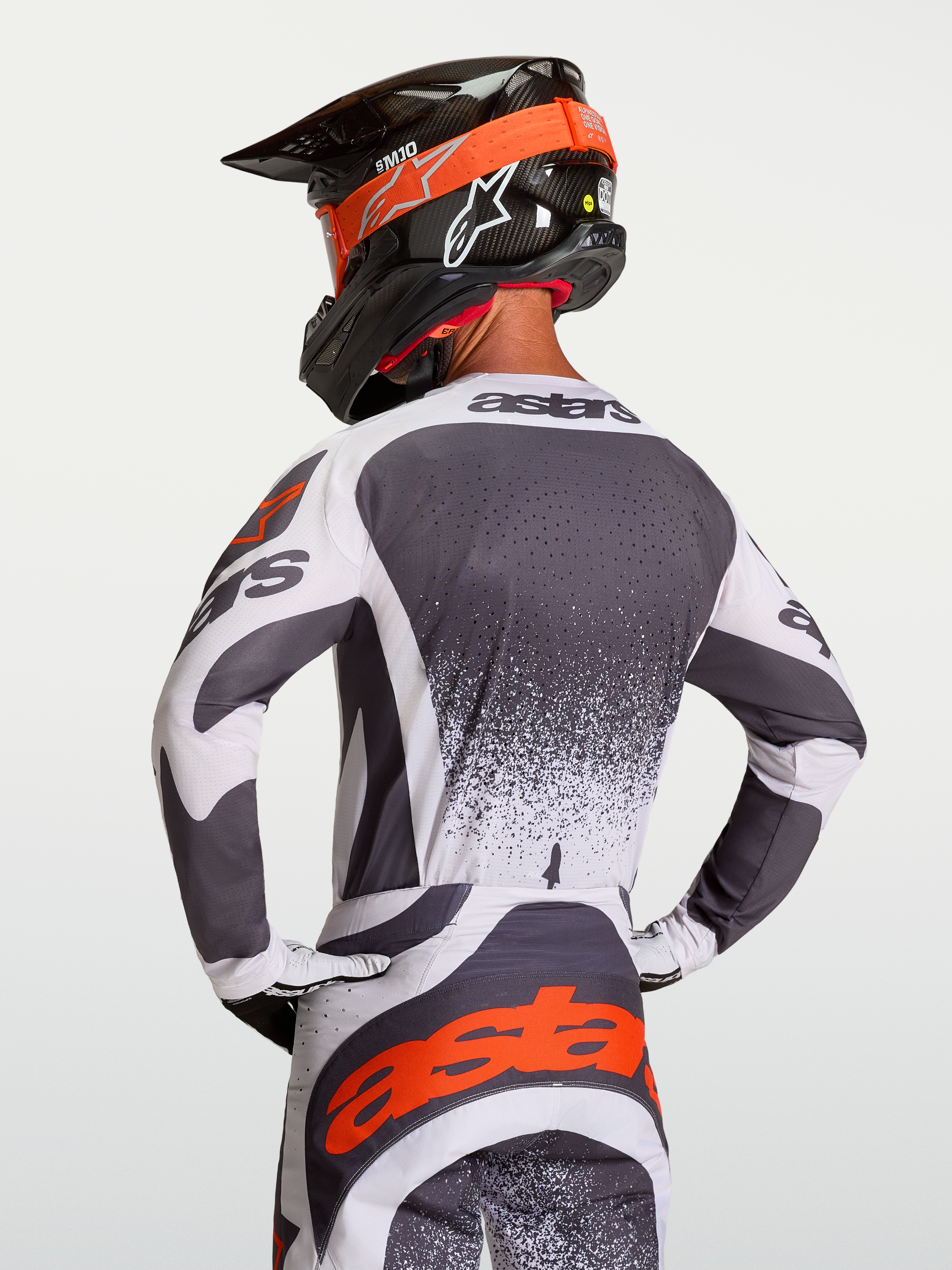 Maillot Alpinestars Techstar Swan, maillot de motocross gris et blanc avec détails rouges, perforations laser, porté par un pilote.