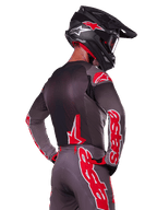 Ensemble d'équipement Supertech Lipan 2025 Alpinestars, pilote de motocross vu de dos, maillot et pantalon gris anthracite avec marquage 'astars' rouge vif sur les manches et le dos, complété par un casque noir