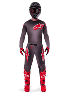 Pilote de motocross portant l'ensemble d'équipement Alpinestars Supertech Lipan 2025, Smoke et Rouge Éclatant, maillot et pantalon gris foncé avec des logos Alpinestars rouges vifs, bottes rouge vif, casque noir et gants rouges, tenue professionnelle coordonnée pour le tout-terrain