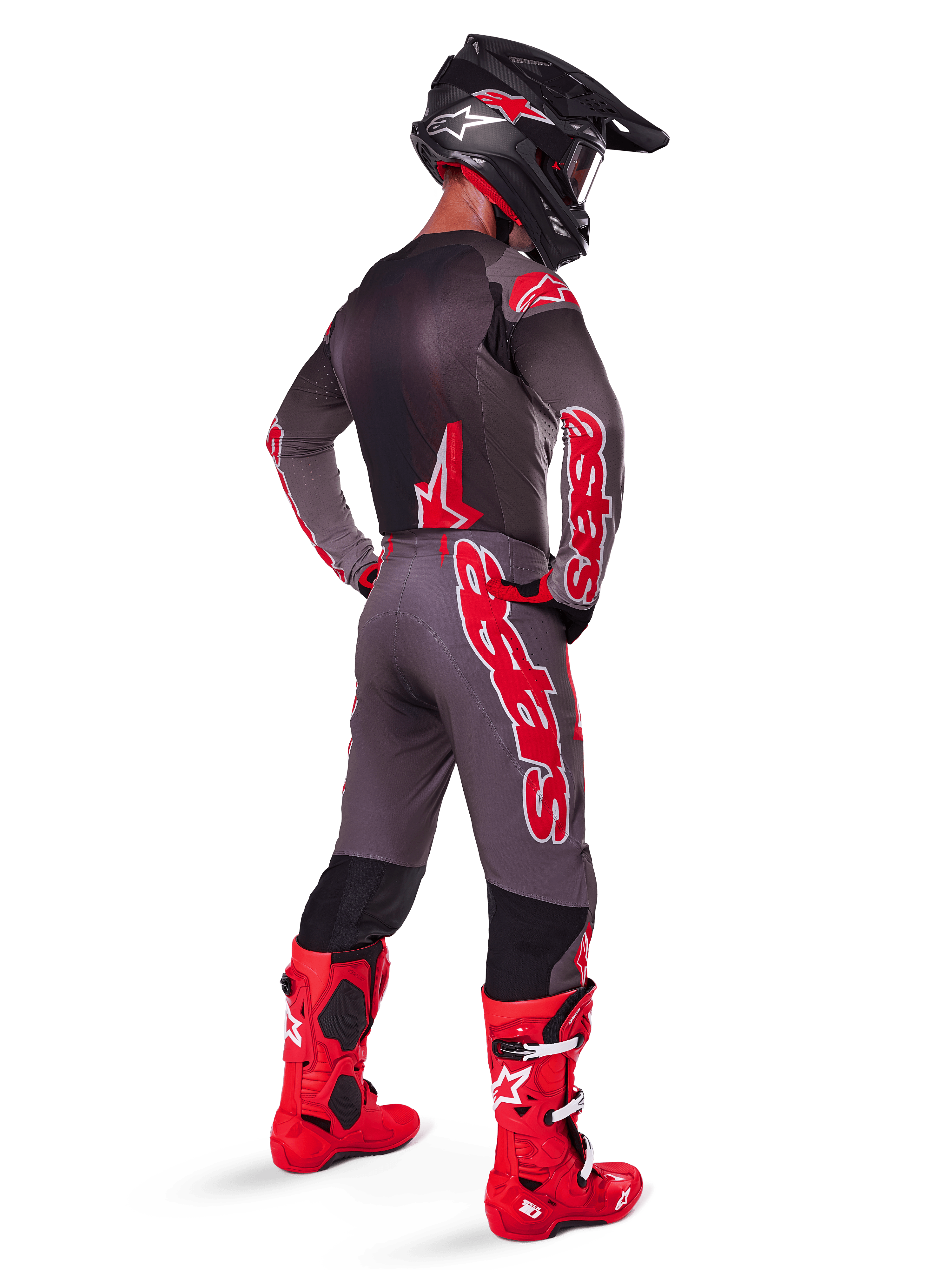 Pilote de motocross portant l'ensemble Alpinestars Supertech Lipan 2025 en Smoke Bright Red, vu de dos, maillot gris et pantalon assorti avec logos Alpinestars rouges, bottes de course rouge vif et casque noir avec logos rouges, tenue de course professionnelle complète pour le tout-terrain