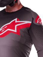 Maillot Alpinestars Supertech Lipan 2025, Smoke Bright Red, vue rapprochée montrant le grand logo étoile rouge et blanc sur la poitrine, des perforations découpées au laser pour la circulation de l'air et un tissu léger et respirant sur un pilote.