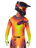 Motocross rider wearing the 2025 Supertech Lipan Jersey, vibrant yellow orange and pink gradient colorway, large black Alpinestars star logo with pink outline on the chest, laser-cut perforations for ventilation, athletic race fit, paired with matching pants, yellow gloves, and a black helmet with goggles.