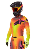 Pilote de motocross portant l'ensemble d'équipement Alpinestars Supertech Lipan 2025, composé d'un maillot avec dégradé jaune et orange et logo Astars rose et noir, de gants jaune fluo et d'un casque noir avec des lunettes rouges, équipement de course tout-terrain professionnel.