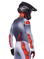 Pilote de motocross vu de dos portant le maillot et l'ensemble d'équipement Alpinestars Supertech Lipan 2025, gris avec des accents orange fluo, logo distinctif sur le dos et les manches, casque noir et gants noirs, tenue de course de motocross coordonnée