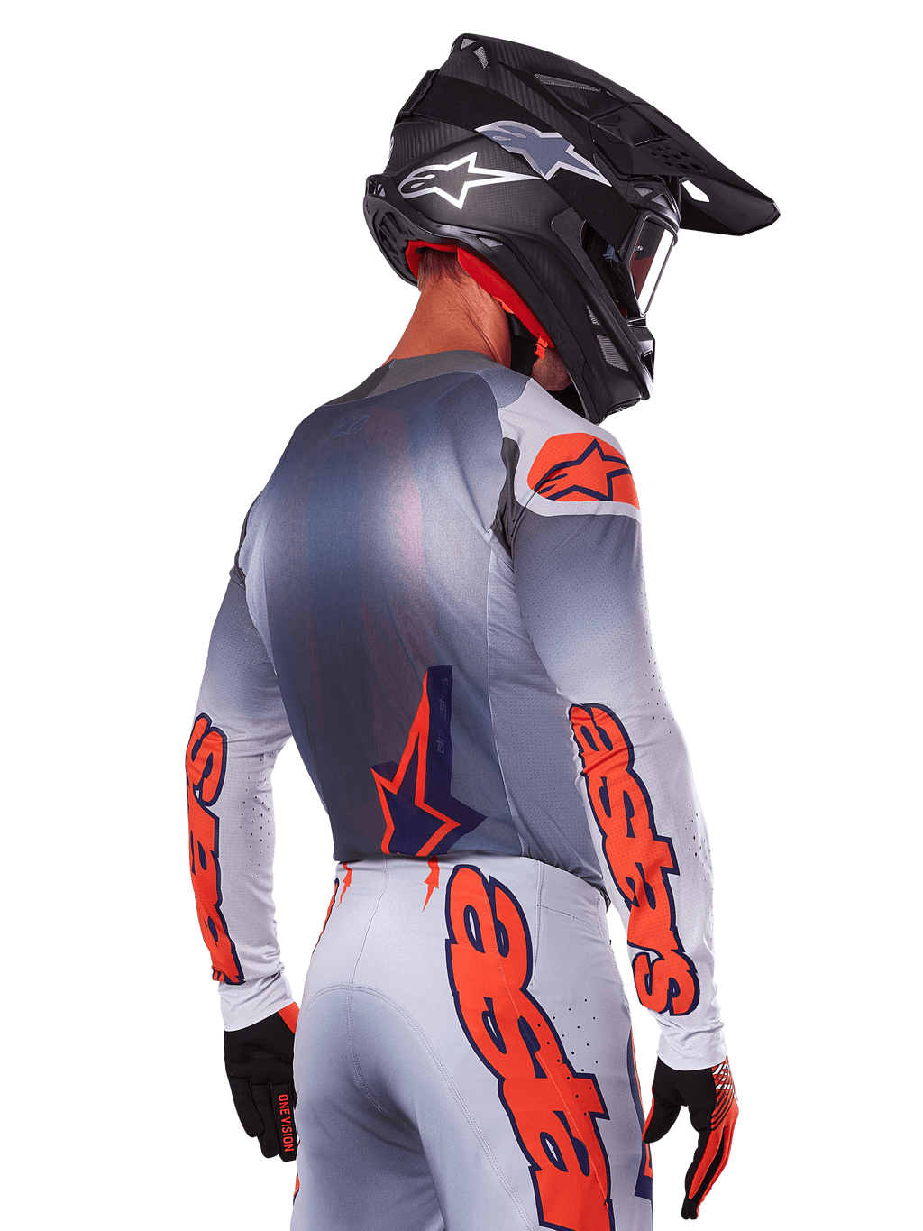 Pilote de motocross de dos portant le maillot Alpinestars Supertech Lipan 2025 en Gris Orange Fluo, avec des logos orange sur les manches et le dos, associé à un pantalon assorti et un casque noir, tenue de course professionnelle pour la performance tout-terrain.