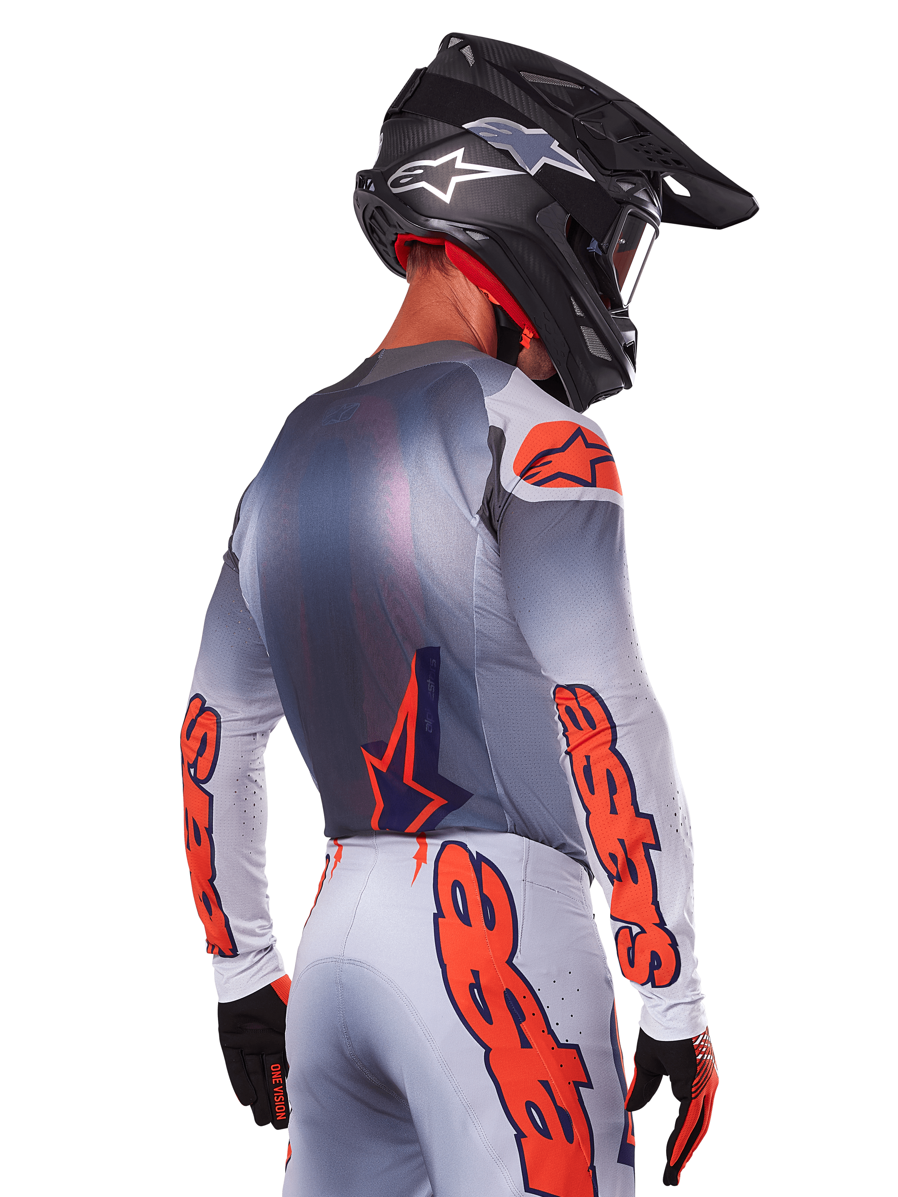 Pilote de motocross de dos portant le maillot Alpinestars Supertech Lipan 2025 en Gris Orange Fluo, avec des logos orange sur les manches et le dos, associé à un pantalon assorti et un casque noir, tenue de course professionnelle pour la performance tout-terrain.