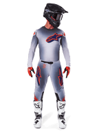 Pilote de motocross portant l'ensemble d'équipement Supertech Lipan 2025 d'Alpinestars en Gris Orange Fluo, comprenant un maillot gris avec accents orange et logo bleu marine, un pantalon gris assorti, un casque noir mat, des bottes blanches et noires et des gants rouges et noirs, tenue de course complète de niveau professionnel
