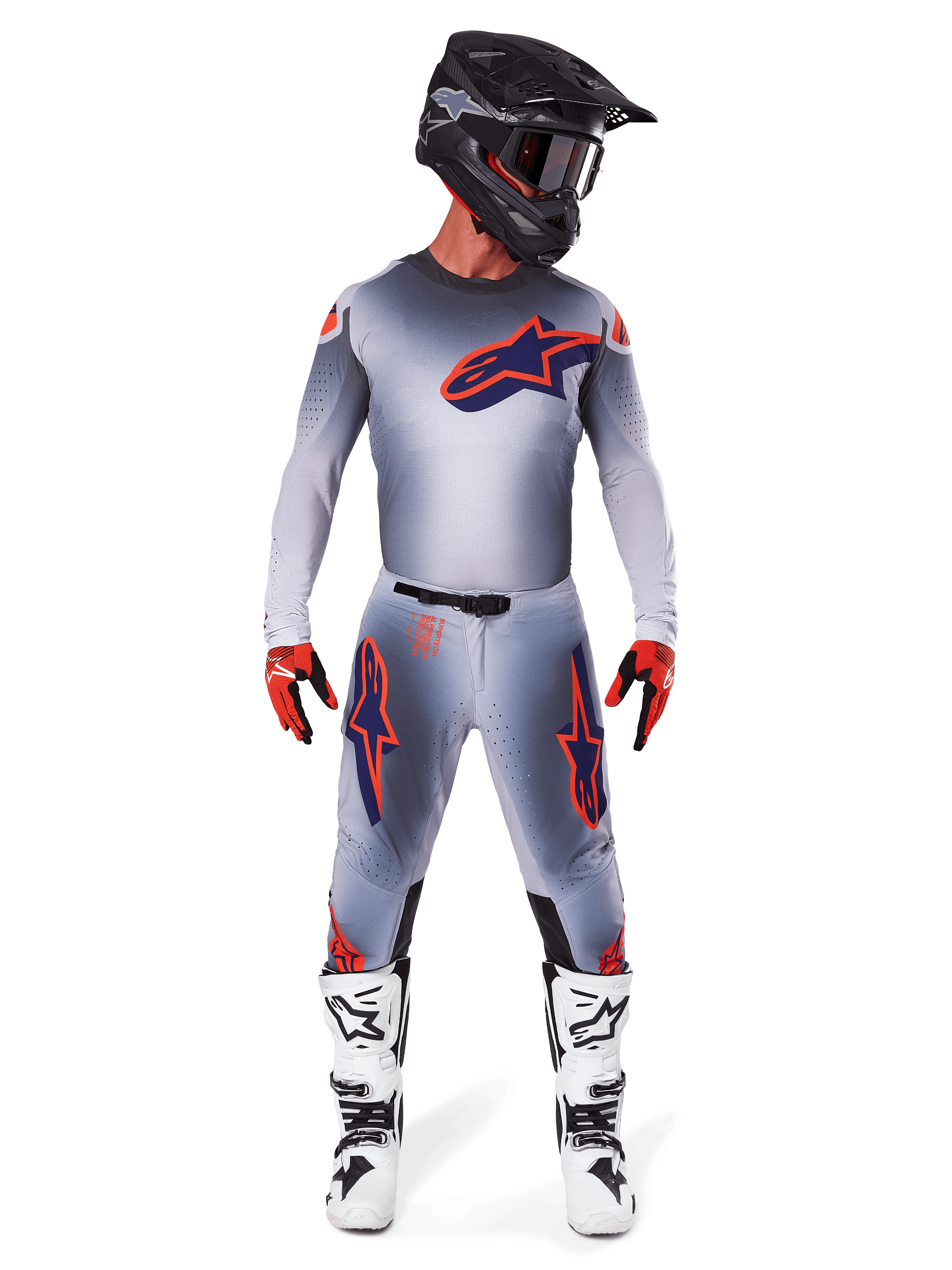Pilote de motocross portant l'ensemble d'équipement Supertech Lipan 2025 d'Alpinestars en Gris Orange Fluo, comprenant un maillot gris avec accents orange et logo bleu marine, un pantalon gris assorti, un casque noir mat, des bottes blanches et noires et des gants rouges et noirs, tenue de course complète de niveau professionnel