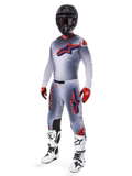 Ensemble d'équipement Alpinestars Supertech Lipan 2025, équipement de motocross, gris avec graphismes d'étoiles orange fluo et bleu marine, porté avec un casque noir, des gants rouges et noirs et des bottes blanches et noires, tenue tout-terrain professionnelle complète au design ventilé