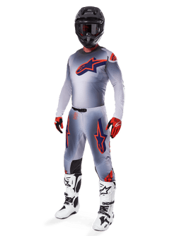 Ensemble d'équipement Alpinestars Supertech Lipan 2025, équipement de motocross, gris avec graphismes d'étoiles orange fluo et bleu marine, porté avec un casque noir, des gants rouges et noirs et des bottes blanches et noires, tenue tout-terrain professionnelle complète au design ventilé